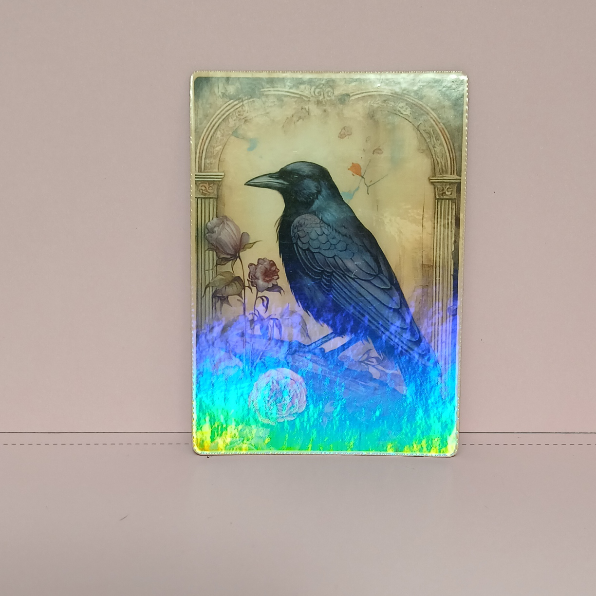 Decorative card with a black crow, flowers, and arch design on a beige background. Sample of TCG card with clear holographic vinyl